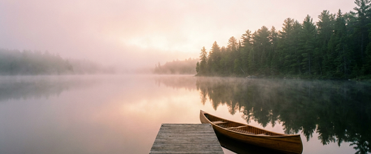 Calm misty lake at dawn with a dock and canoe