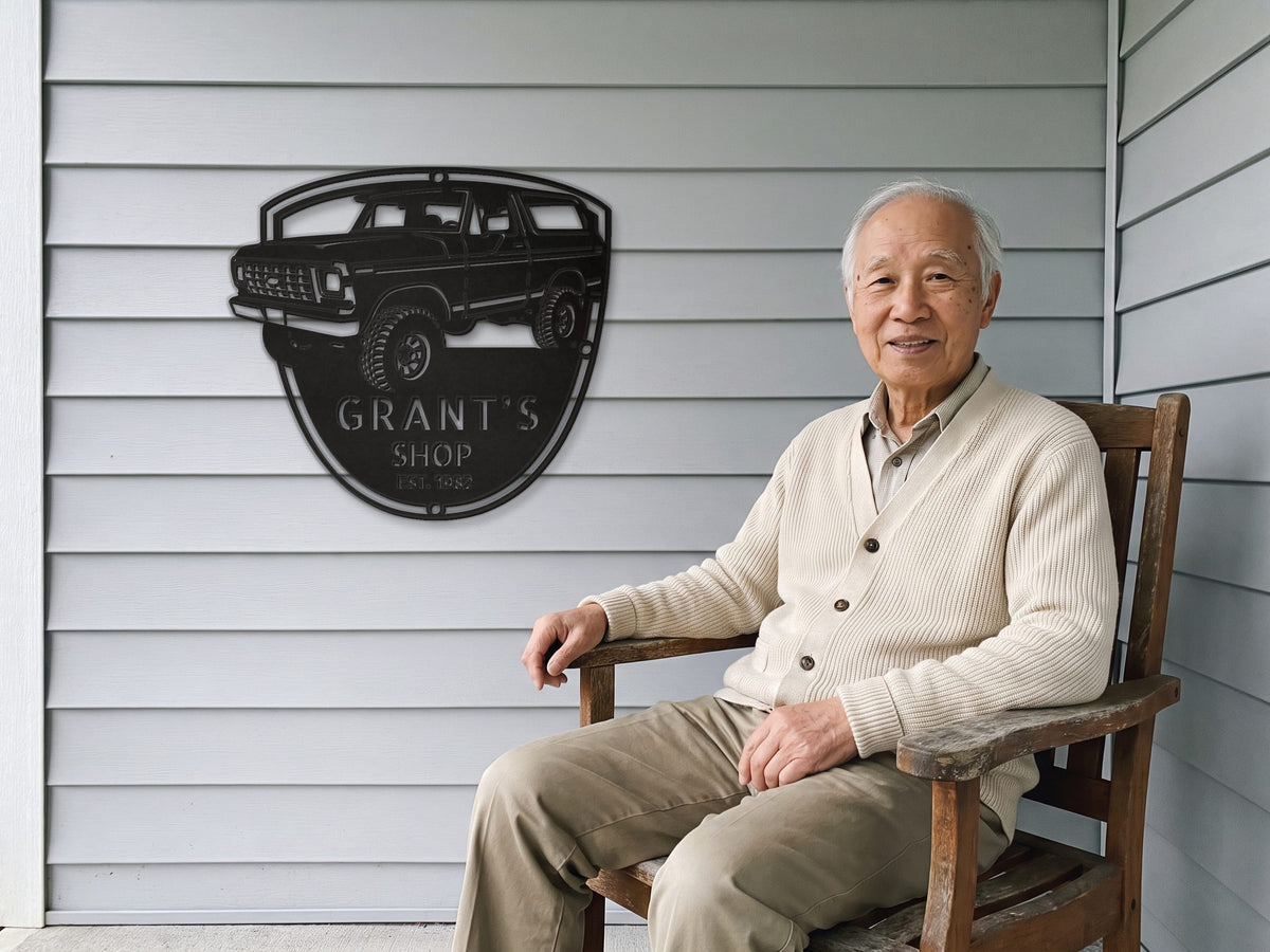 Grandpa on the porch beside his 78 Bronco shop sign with name and EST year