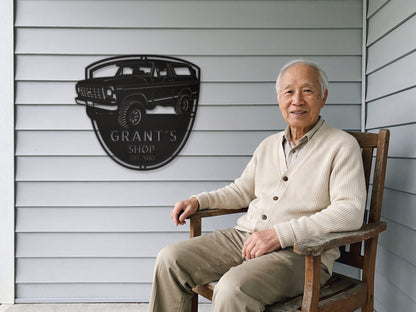 Grandpa on the porch beside his 78 Bronco shop sign with name and EST year