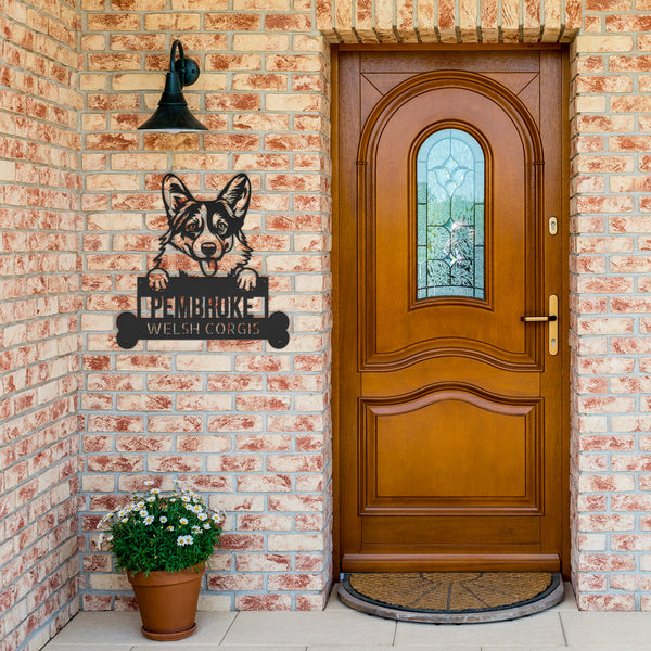 A wooden front door with an arched window is set in a brick wall. A potted plant sits beside the door, and a Pembroke Welsh Corgis Dog Sign, Custom Metal Wall Art, Personalized Pet Name Sign for Home Decor, Unique Gift for Dog Lovers hangs nearby.