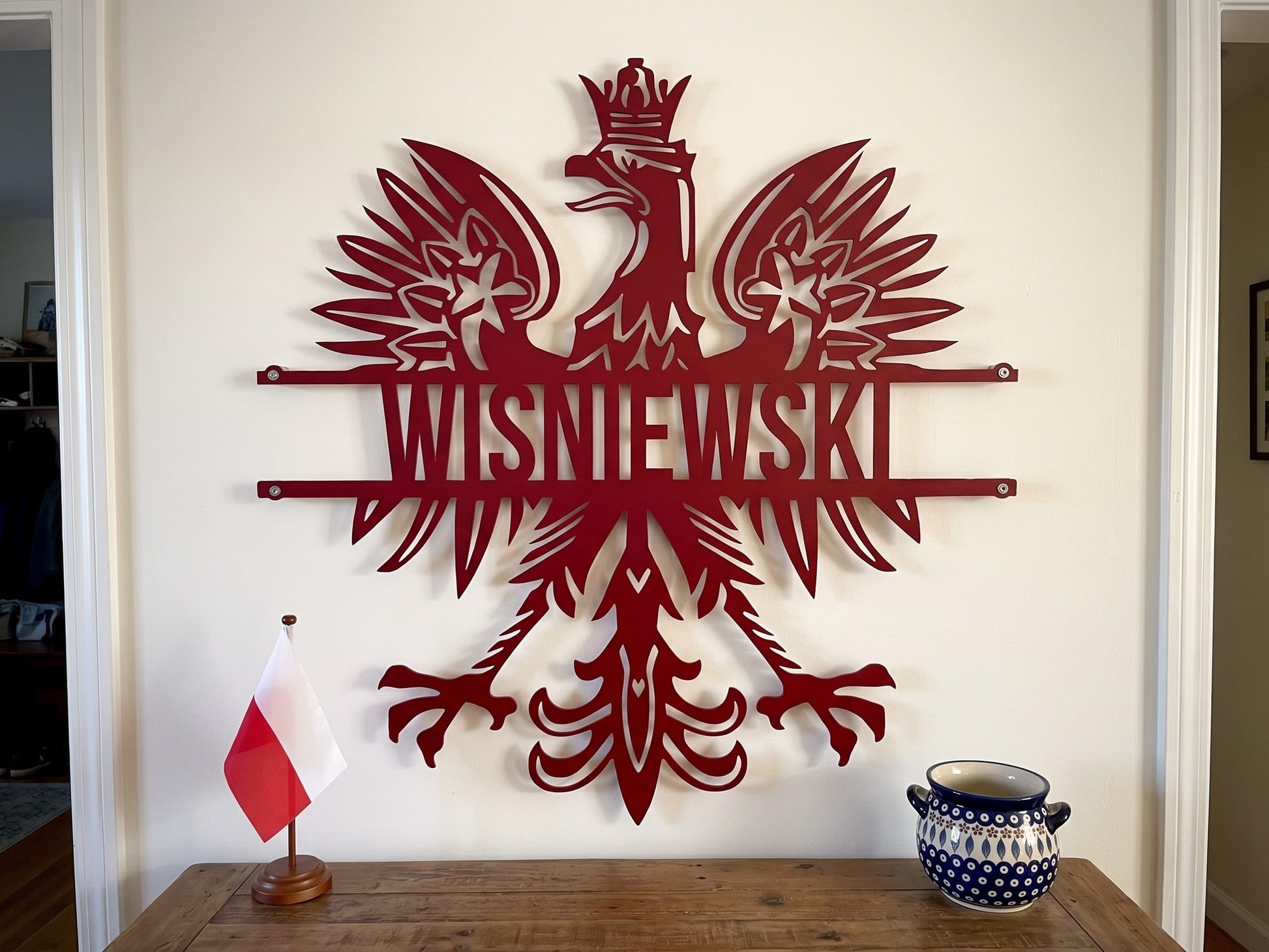 Polish eagle metal sign in red on an entry wall beside a Polish flag and Boleslawiec pottery, WISNIEWSKI