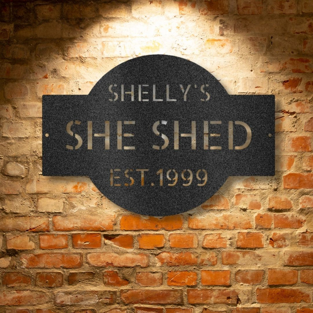 A PERSONALIZED Metal Wall Art Decor plaque that says she shed on a brick wall.