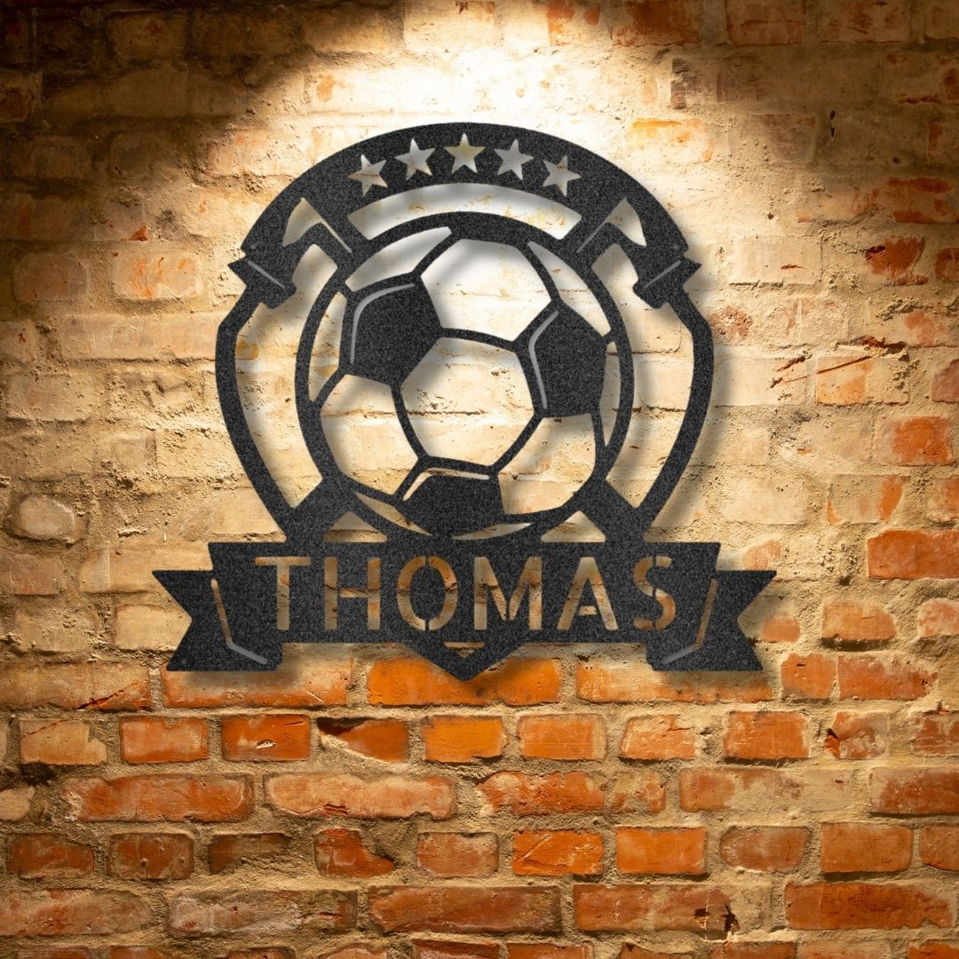 A personalized steel monogram of the name Thomas, displayed as a soccer plaque, adorning a brick wall.