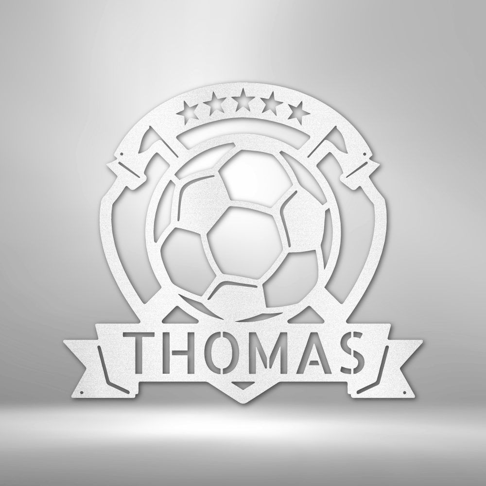 A personalized steel monogram of the name Thomas, displayed as a soccer plaque, adorning a brick wall.