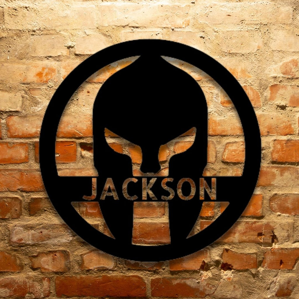 A Durable Outdoor Metal Sign featuring a Custom Handmade Design of a Spartan Helmet with the name Jackson on a brick wall.