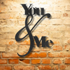 Metal Wall Art Decor - You and Me Quote on a steel sign displayed on a brick wall.